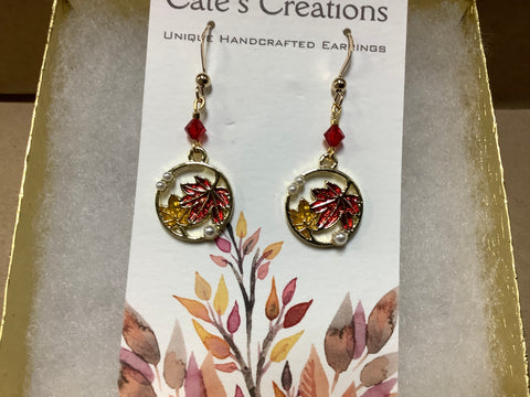 2 maple leaves in center of round gold with little beads on outer edge. Drop earring with a red bead,  with plated gold findings.