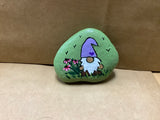 Gnome with pink flower in grass with background green rock. Made by local artist Cecelia. Each rock is $3.