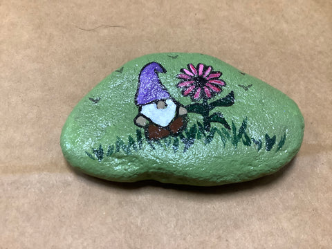 Gnome with pink flower in grass with background green rock. Made by local artist Cecelia. Each rock is $3.