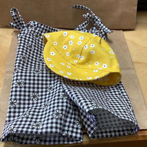 Gingham checked romper with daisy’s and a yellow cap.