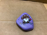 Hand Painted Rock of Gnome by a flowers standing in grass by local artist Cecelia.
