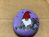 Hand Painted Rock of Gnome by a flowers standing in grass by local artist Cecelia.